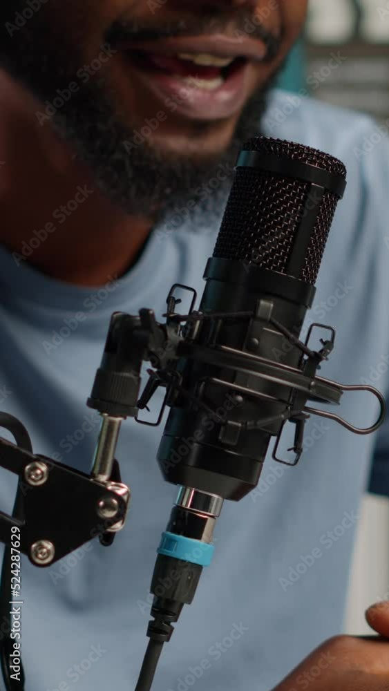 Poster vertical video: close up of influencer using microphone to talk on online podcast in studio. vlogger