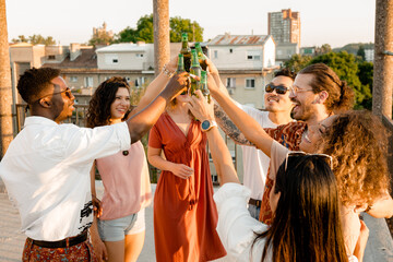 The multiracial friends are toasting with beer at the rooftop party.