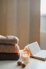 cozy comfortable home autumn still life with a candle, book, knitted sweaters and plaid