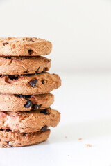 Close up of a stack of six delicious chocolate chip cookies on white table with biscuit crumbs