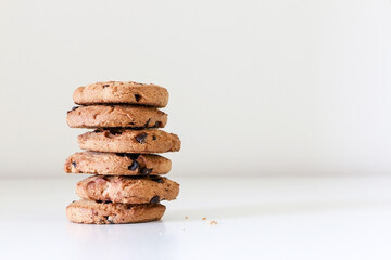 A stack of six delicious chocolate chip cookies on white table, tasty biscuit snack, left of frame, copy space on right