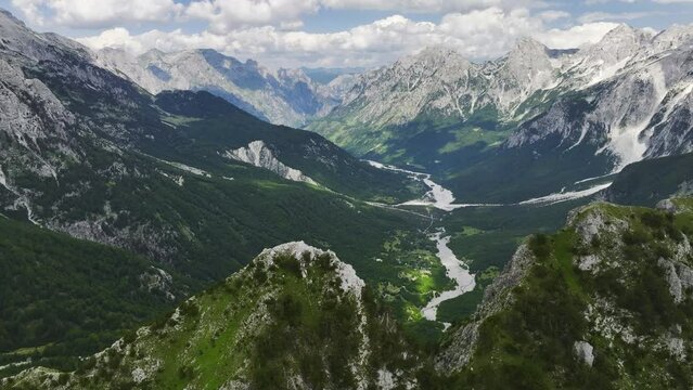 Aerial view of the Valbona river valley, green valleys, blue sky with clouds, steep rocks, remnants of snow. Hikers paradise. Theth national park, june, Albanian Alps, Albania.