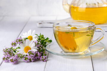 Herbal tea with chamomile and thyme in a transparent cup on a white wooden table