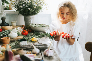cute little girl in casual white dress sit near table on veranda of country village house with different vegetables, eco-friendly food from garden, autumn harvesting