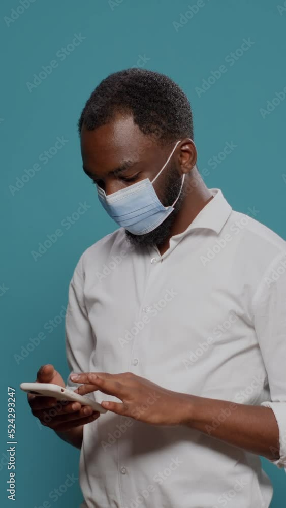 Poster vertical video: male entrepreneur using smartphone to browse internet, wearing face mask in studio. 