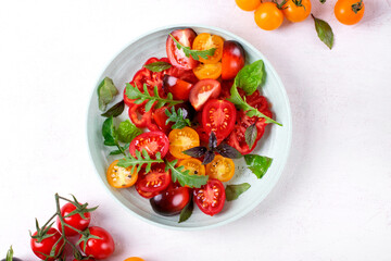 Salad with red, black and yellow cherry tomatoes, arugula and basil dressed with black salt and olive oil served on wheat straw plate. Top view