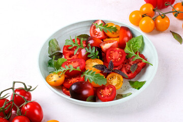 Salad with red, black and yellow cherry tomatoes, arugula and basil served on wheat straw plate. Healthy eating