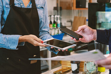 female barista uses a tablet to accept mobile payments from customers. At the counter in cafes and restaurants