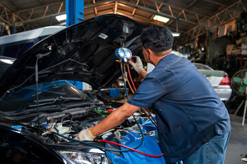 Asian senior mechanic man or technician use tools to monitor pressure and gas of car engine and he...