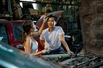 Asian mechanic woman tease or action fun with her co-worker in garage in front of engine of the car.