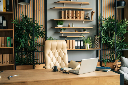 Modern office of general manager, businessman, ceo. Stylish wooden table, leather chair, interior. Workplace, workspace of accountant, financial director. Shelves with documents. Home library