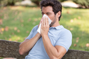 man suffering from hayfever outdoors blowing nose