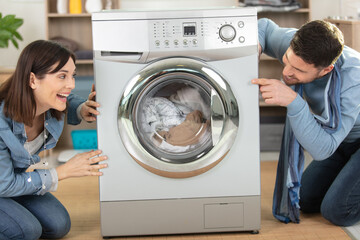 happy couple using new washing machine at home - obrazy, fototapety, plakaty