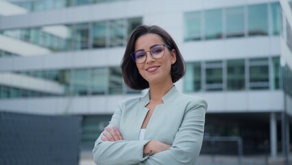 Fototapeta premium Front closeup portrait of young businesswoman with brown hair standing on street, looking friendly at camera