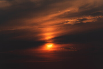 Dramatic apocalyptic scene of bright orange sun behind sinister dark clouds, hope in darkness