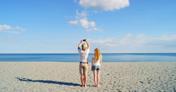 Selfie, romance and young couple at beach with phone taking photo at the beautiful spring ocean or sea. Man and woman bonding on romantic holiday travel, summer getaway or vacation together.