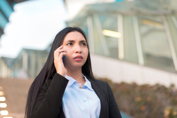 A worried corporate employee talking on the phone with her workmate about a problem their company is facing. An upset woman in corporate attire being scolded by her boss on the phone at noon.