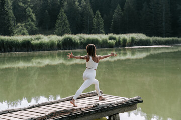Fototapeta na wymiar Eine Junge Frau praktiziert Yoga auf einem Steg am See zum Sonnenaufgang. Der Felixer Weiher - Tretsee in Südtirol. Weiße Leggins 3