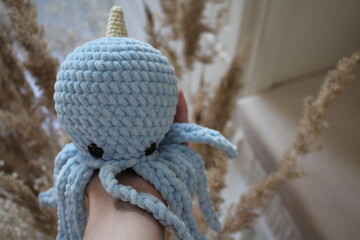 knitted blue toy octopus in the interior of pastel colors, girl holding in hand 