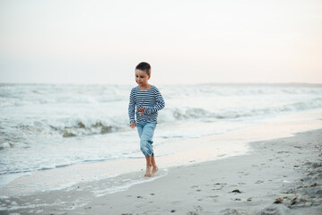 Boy in a striped T-shirt at the seaside. Child running on the beach. Summer vacation. happy kid playing on beach at the sunset time