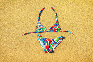 Fototapeta na wymiar Colorful swimsuit lying down on the golden sandy beach. Copy space. Top view.
