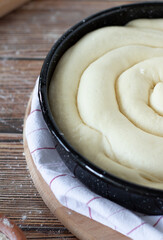 Unbaked dough pie in a round pan ready for baking on a wooden table dusted with flour and a kitchen cloth. A close-up. Vertical shot, selective focus.