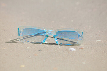 Fototapeta na wymiar blue sunglasses from the sun lie on the sand near the sea in sunny weather