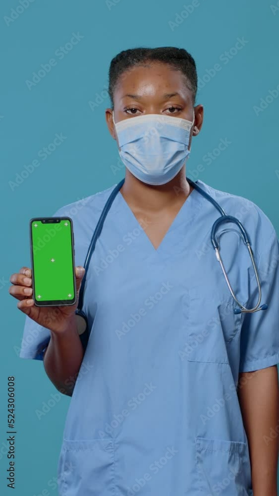 Poster medical assistant vertically holding smartphone with green screen and looking at camera. nurse with 