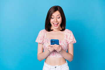 Photo portrait of lovely young woman hold device excited use new app wear stylish flower print clothes isolated on blue color background