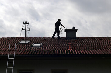 Ein Kaminkehrer säubert auf einem Hausdach den Kamin