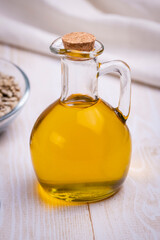 Sunflower vegetable oil in a glass vessel and sunflower seeds on a wooden background.