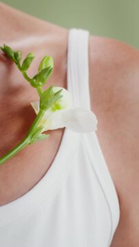 An elderly woman strokes her neck with a white flower, close-up, no face, vertical video