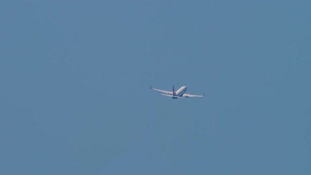 Commercial Airliner gaining altitude after takeoff in the blue sky. Rear view long shot, plane turning