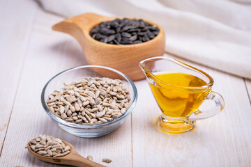 Sunflower vegetable oil in a glass vessel and sunflower seeds on a wooden background.