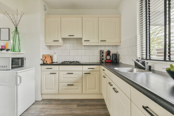 Well organized small home kitchen interior with sink under window and light furniture with stove...