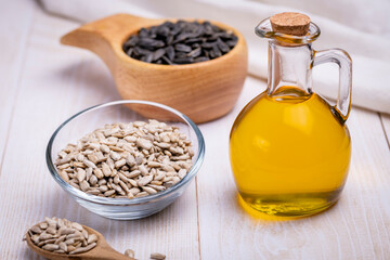 Sunflower vegetable oil in a glass vessel and sunflower seeds on a wooden background.