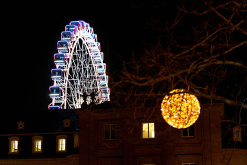 Ferris wheel behind historical building at night. Christmas decoration on a tree.