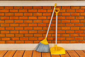 Long handle plastic yellow broom and dustpan prop against a red brick wall of a house. - obrazy, fototapety, plakaty