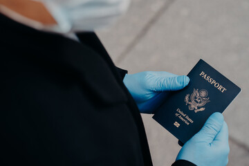 Unknown man tourist wears rubber medical gloves, holds passport, cannot travel during pandemic...