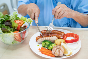 Asian senior or elderly old lady woman patient eating breakfast and vegetable healthy food with hope and happy while sitting and hungry on bed in hospital.