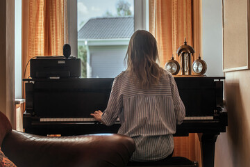 a young beautiful woman sits with her back to us and plays the piano, music lessons in young people