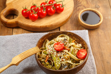 Udon with vegetables and mushrooms on the table in a wooden plate next to champignons and tomatoes on a plank.