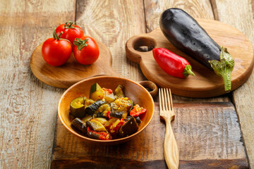 A plate of grilled vegetables next to tomatoes and eggplant on wooden boards.