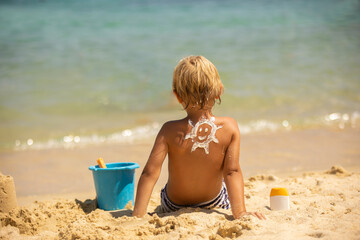 Happy child, blond boy on the beach with applied sun screen,  enjoying summer, playing