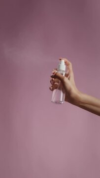 Close-up of female hands spraying liquid from a transparent jar, vertical video on a monochrome background in the studio