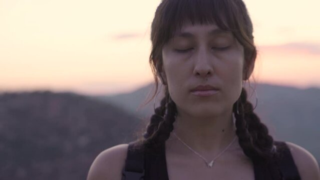 Young Native American woman takes a deep breath with her eyes closed and opens them while looking at the camera. 