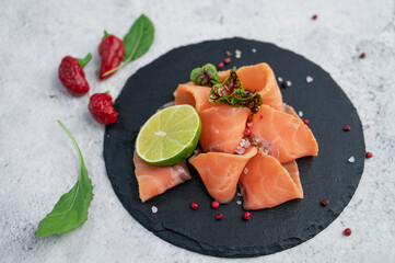 Fresh salmon slices with peppers, greens and lime on concrete background