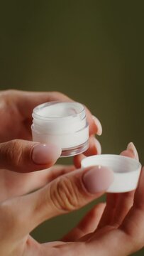 Close-up of female hands opening a small jar of cream, vertical video on a monochrome background in the studio