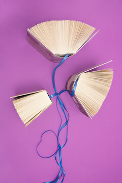 Old books and blue ribbons on bright purple background. Education, knowledge or nature concept. Flat lay. For book lovers.