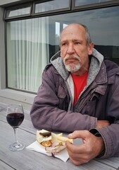 Old man sitting at a table in his garden, enjoying snack and a glass of red wine